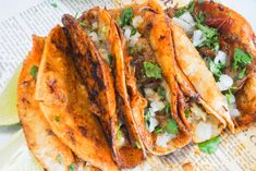 three tacos with meat, onions and cilantro sitting on top of a newspaper