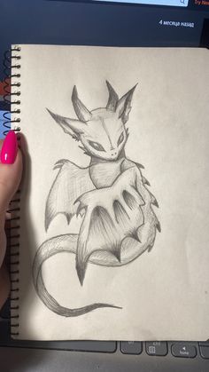 a hand holding a pencil drawing of a dragon