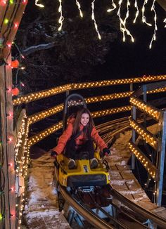 a woman is riding on a roller coaster in the snow with christmas lights around her