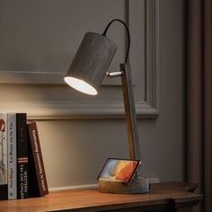 a desk lamp sitting on top of a wooden table next to books and a phone