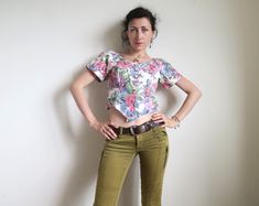 Super-cute 80's cropped blouse with short sleeves. Made in USA by S. L. Petites. Blooming roses painting print in soft pink and blue on white. Buttons down the front. Fabric: 100% cotton. Short raglan sleeves. Cropped length and pointed waist. Tagged size US10. Estimated size XS to S, the model is size XS, please make your judgement from the measurements below: armpit  ~ 90 cm  /  ~ 35 " waist  ~ 78 cm  /  ~ 30 " length  ~ 43 cm  /  ~ 17 " by the back In great vintage condition. Fitted Short Sleeve Cropped Shirt For Spring, Fitted Cropped Shirt With Short Sleeves For Spring, 90s Style Short Sleeve Crop Top For Summer, Vintage Short Sleeve Crop Top For Spring, Vintage Short Sleeve Crop Top For Summer, Retro Short Sleeve Crop Top For Spring, Vintage Fitted Cropped Top, Fitted Vintage Cropped Top, Fitted Cropped Vintage Crop Top