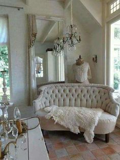 a white couch sitting in front of a window next to a chandelier and mirror