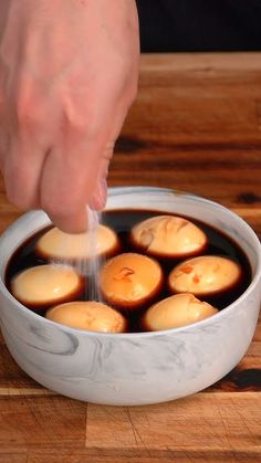 a person is sprinkling some kind of sauce in a white bowl on a wooden table