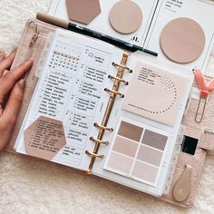 an open planner book with pink and brown items in it on a white rug next to a hand holding a pen