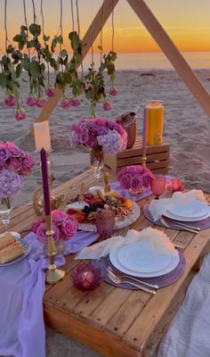 the table is set with flowers and plates for an outdoor dinner on the beach at sunset