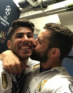 two men who are kissing each other in front of a wall with the words real madrid on it