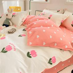 a bed with pink and white sheets, pillows and stuffed animals on the headboard