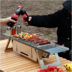 two people are cooking on a grill with drinks and food in the foreground, while another person holds a bottle of coke