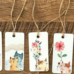 four tags with watercolor cats and flowers hanging from twine on a wooden table