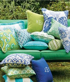 a green couch with pillows on it in front of some bushes and trees, one is blue and the other is green