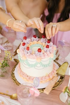 a woman is cutting into a cake with cherries on the top and pink flowers on the bottom