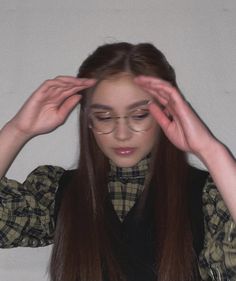 a young woman with glasses is holding her hair in front of her face and looking at the camera