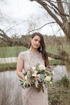 a woman standing in front of a pond holding a bouquet