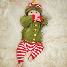 a baby laying on top of a white blanket wearing a green sweater and red striped pants