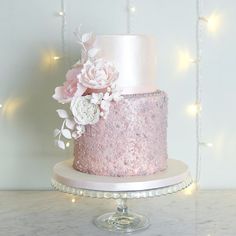 a pink and white wedding cake with flowers on the top is sitting on a pedestal