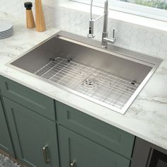 a stainless steel sink in a kitchen with marble counter tops and green cabinets, along with plates and utensils