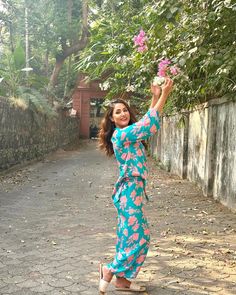 a woman in a blue and pink floral print dress holding flowers up to the sky