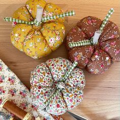 four fabric pumpkins sitting on top of a wooden table next to scissors and thread