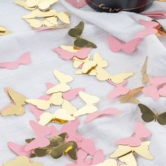 some pink and gold butterflies on a white table cloth next to a bottle of wine