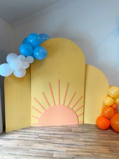 balloons are on the floor in front of a yellow backdrop with an orange and blue balloon arch