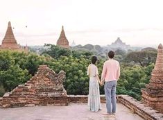 a man and woman standing on top of a stone structure looking out over the trees