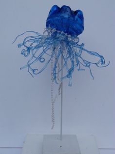 a blue jellyfish sculpture on a white pedestal with chain hanging from it's neck