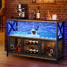 an illuminated bar with bottles and glasses on the top, in front of a brick wall