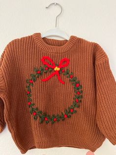 a brown sweater with a red bow on the front and green leaves on the back