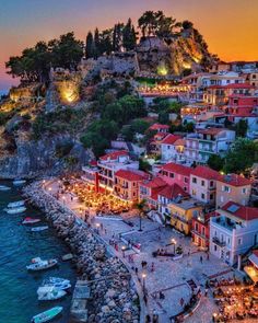 the town is lit up at night by the water with boats parked on the shore