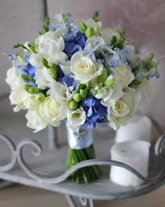 a bouquet of white and blue flowers in a vase on a metal stand next to a mirror