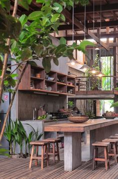 an image of a kitchen with wooden tables and stools on the bottom floor, surrounded by greenery