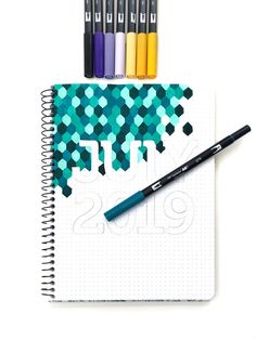 a notebook with markers and pens on top of it, next to some colored pencils