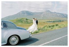 a bride and groom standing next to an old car on the side of the road