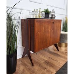 a wooden cabinet sitting on top of a hard wood floor next to a potted plant