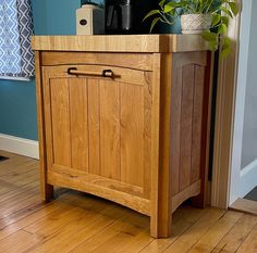 a wooden cabinet sitting on top of a hard wood floor next to a potted plant