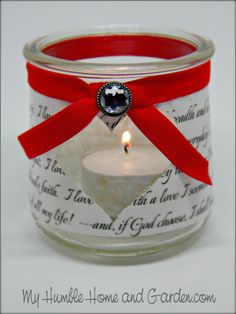 a candle in a glass jar with a red ribbon around the edge and a heart on it