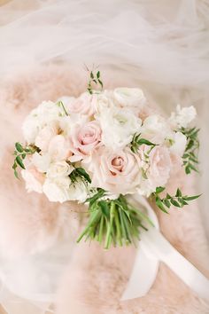 a bridal bouquet with white and pink flowers on a fur - lined surface,