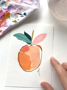 a hand holding an orange on top of a piece of paper