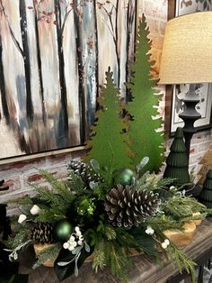 a fireplace mantel decorated with pine cones, evergreens and other greenery in front of a painting