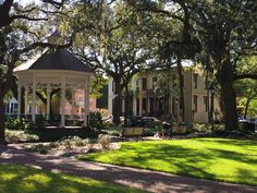 a gazebo sitting in the middle of a lush green park next to tall trees