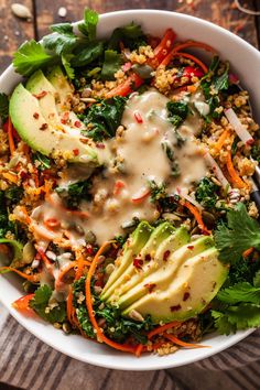 a white bowl filled with salad and dressing on top of a wooden table next to a fork