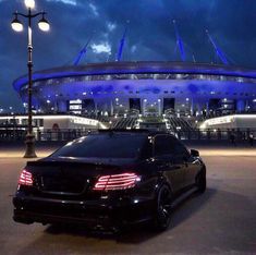 a black car parked in front of a large building with lights on it's sides