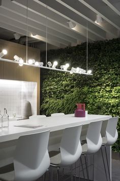 a kitchen with white chairs and a green wall behind the counter top, along with lights hanging from the ceiling