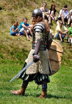 a man dressed in armor and holding a wooden barrel while standing on top of a lush green field