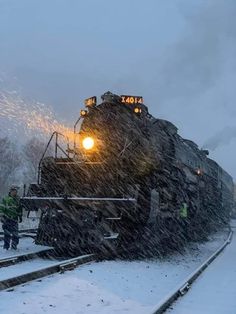 a train traveling through snow covered countryside next to tracks and people standing on the platform