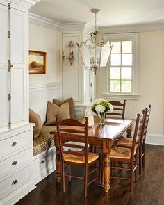 a dinning room table with chairs and a bench in front of the window is surrounded by white cabinets