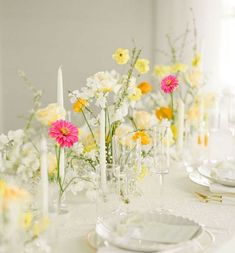 the table is set with white and yellow flowers in vases, candles, and plates