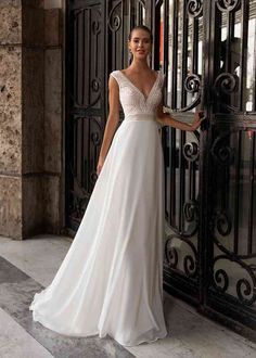 a woman standing in front of an iron gate wearing a white dress with beading