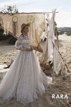 a woman in a white dress and hat standing on the beach next to a tent