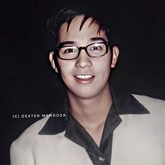 a young man wearing glasses and a white blazer smiles at the camera while standing in front of a black background